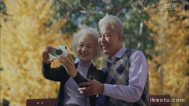 幸福的老年夫妇坐在户外用手机拍照